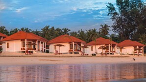 A row of beachside cottages with red roofs and white walls, each with a small porch and seating area. - Ngapali Paradise Hotel (Thandwe)