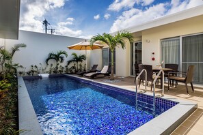 A swimming pool with lounge chairs and a table, surrounded by plants and a palm tree. - Ahman Suite Villa Sumuide (Nago)
