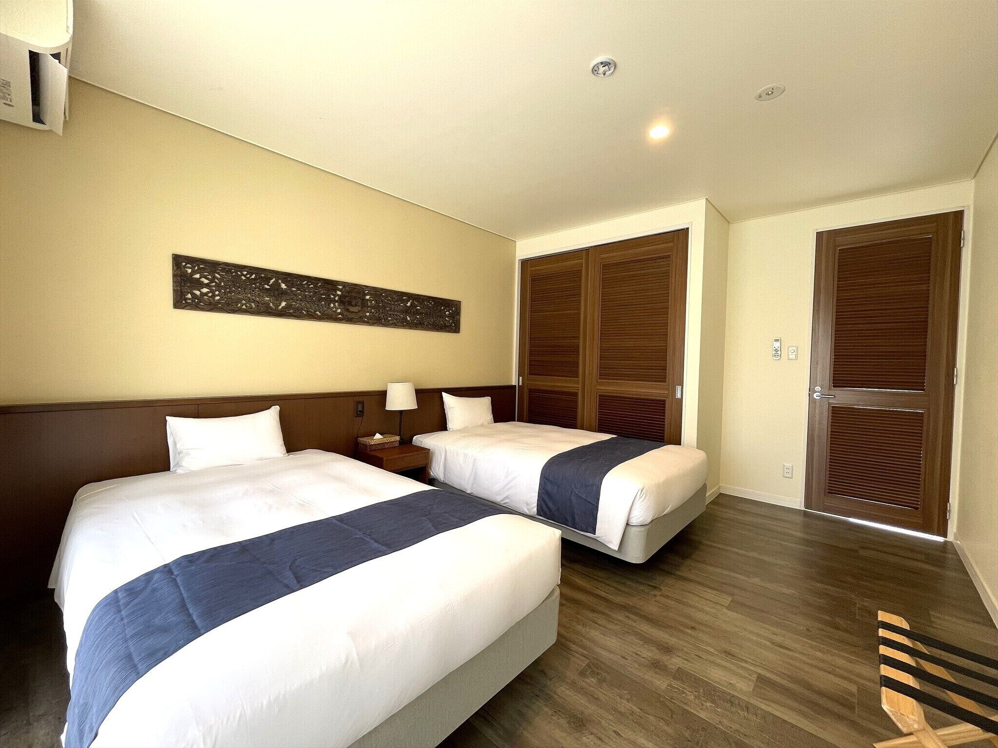A hotel room with two beds, wooden flooring, a decorative wall piece, and a wooden wardrobe.