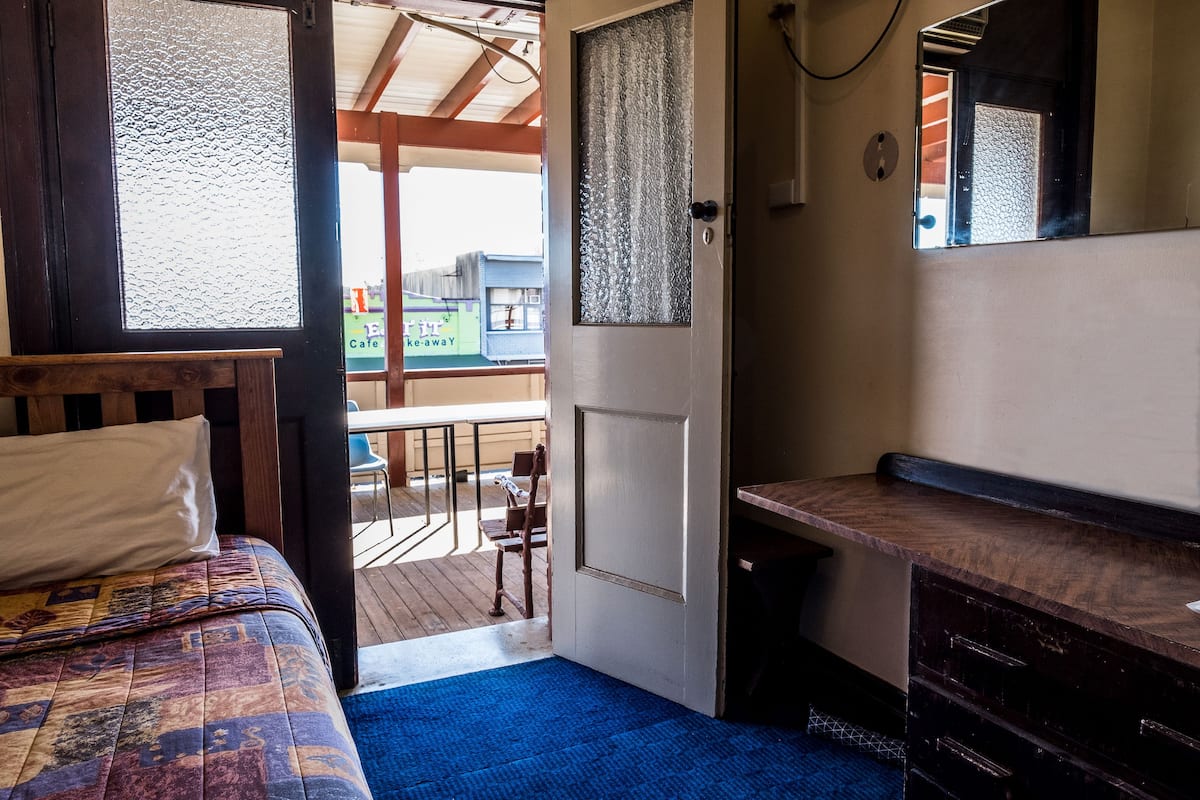 A room with a bed, a desk, and a view of an outdoor deck.