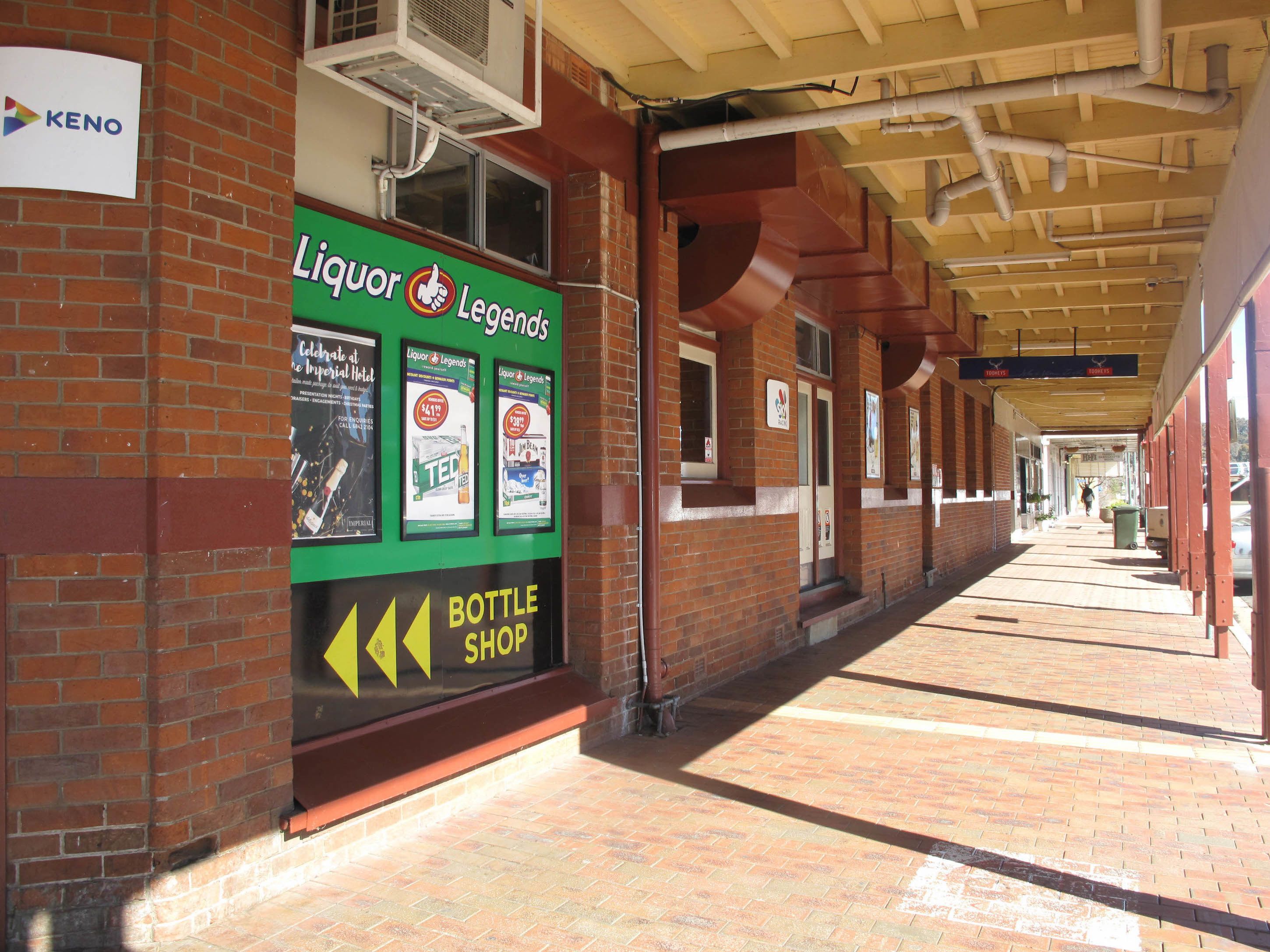 A brick building with a covered walkway, a liquor store named 'Liquor Legends' with promotional posters, and a KENO sign.
