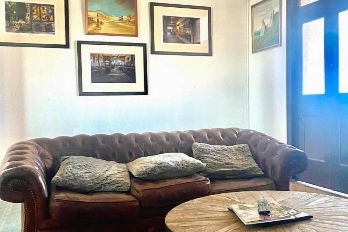 A room with a brown leather sofa, a round wooden coffee table, and framed pictures on the wall.