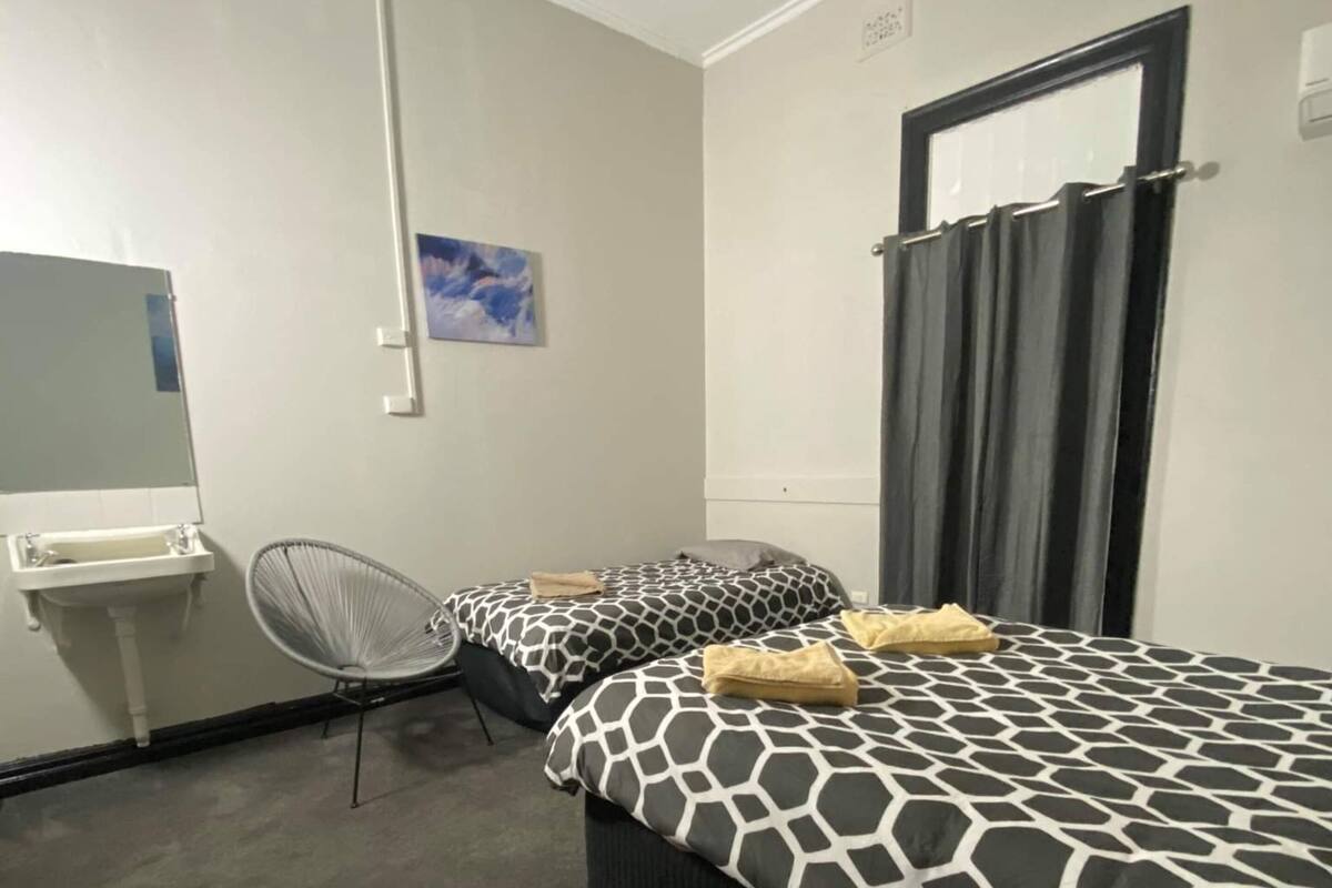 A room with two beds, a chair, a sink, and a mirror.