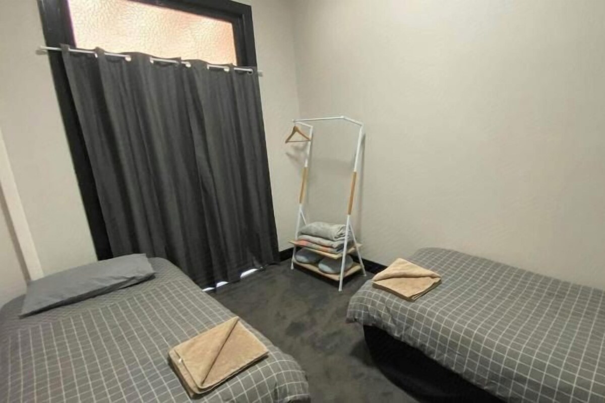 A room with two beds, a wardrobe, and a drying rack.