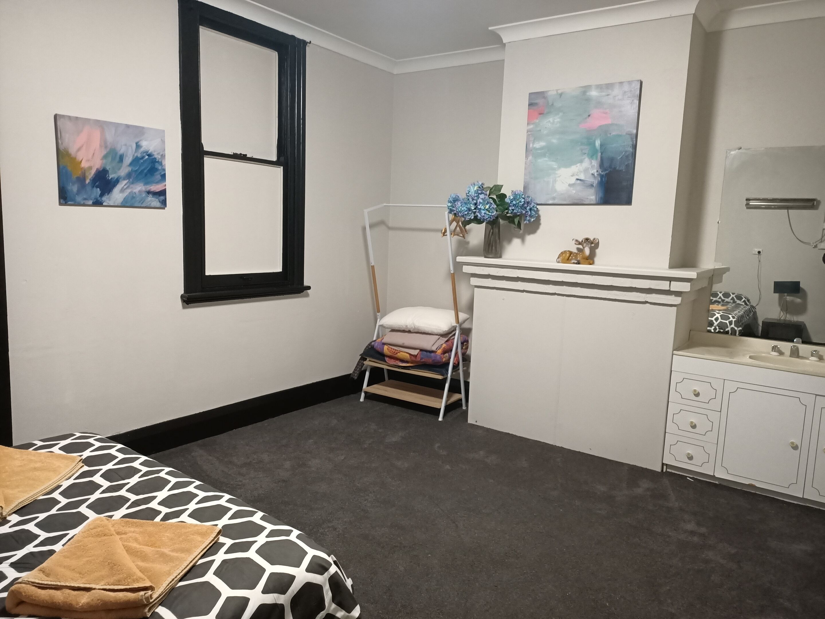 A bedroom with a bed, a nightstand, a dresser, a mirror, and two abstract paintings on the walls.