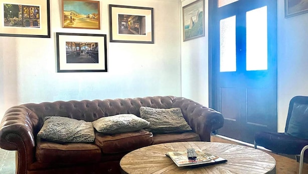 A living room with a brown leather sofa, a round wooden coffee table, and framed pictures on the wall. - Imperial Hotel Coonabarabran (Coonabarabran)