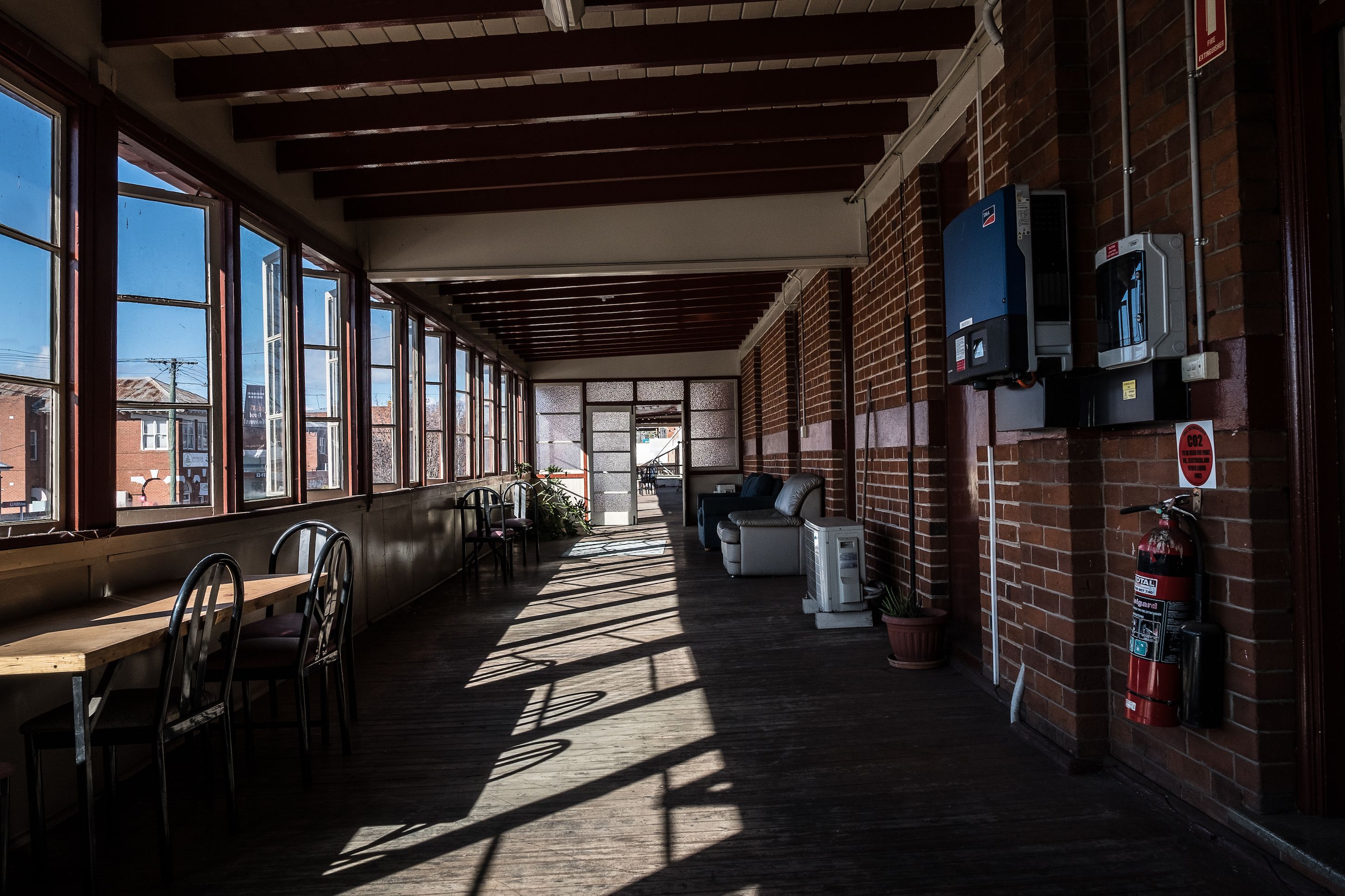 A long corridor with wooden benches and tables, large windows, and brick walls.