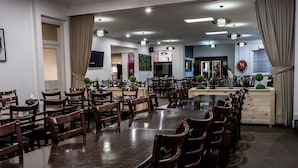 A spacious dining area with multiple wooden tables and chairs, a kitchen area in the background, and a large window with curtains. - Imperial Hotel Coonabarabran (Coonabarabran)