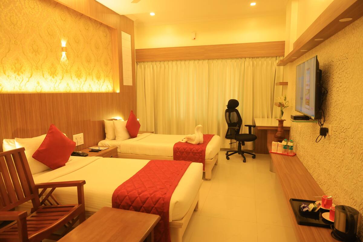 A hotel room with two beds, a wooden desk, a chair, a TV, and a small table with a tray.