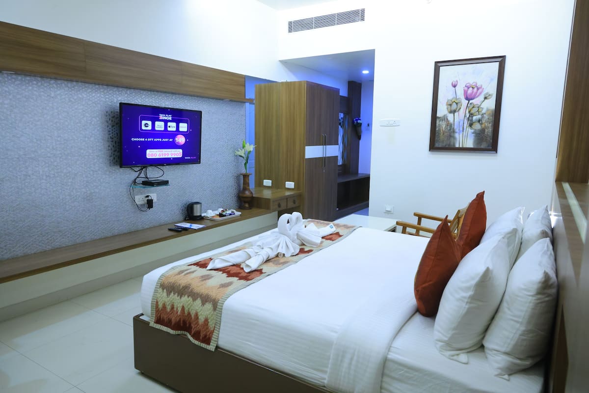 A hotel room with a bed, a television, a painting, and a wooden wardrobe.
