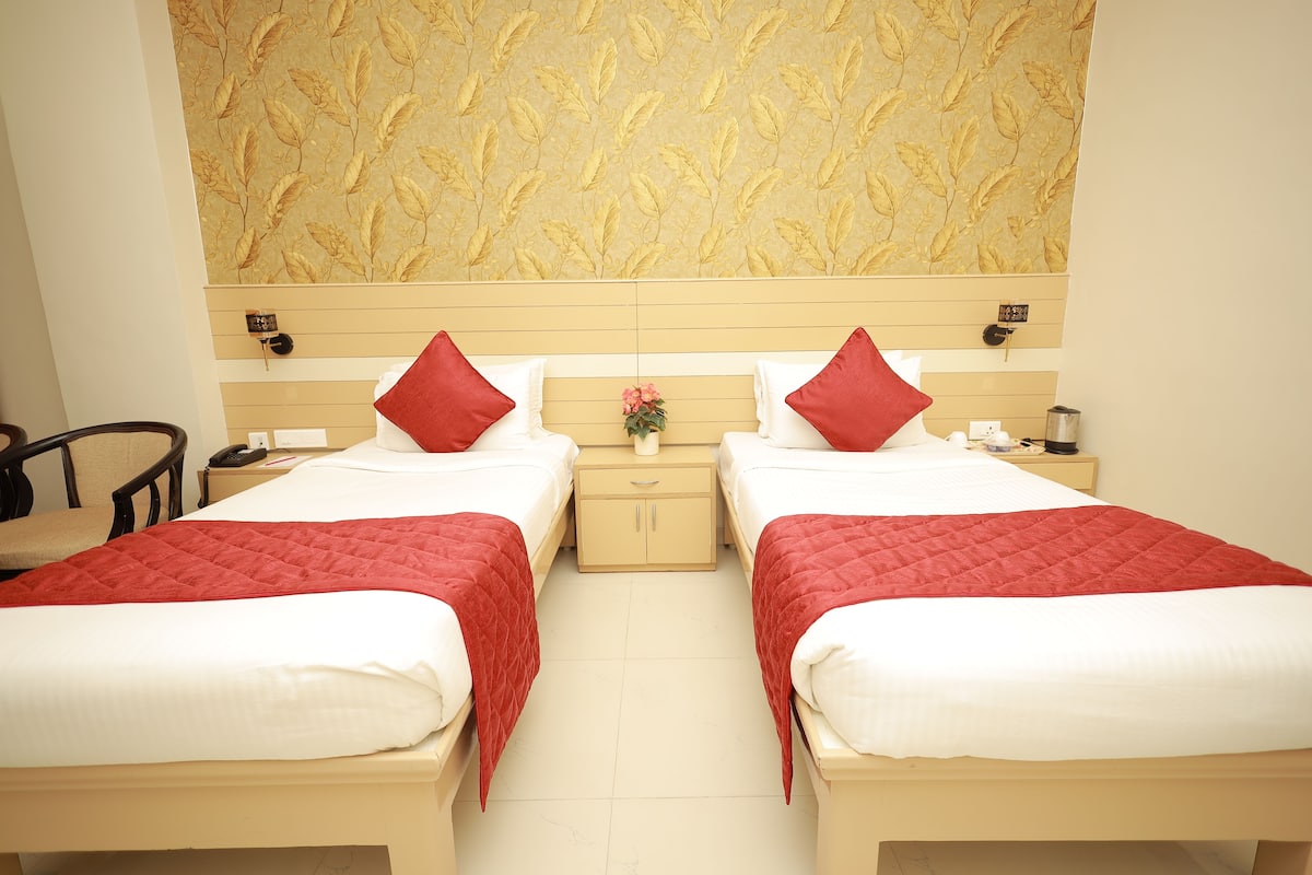 A hotel room with two beds, each with red and white bedding, a small bedside table with a lamp, and a wall clock.