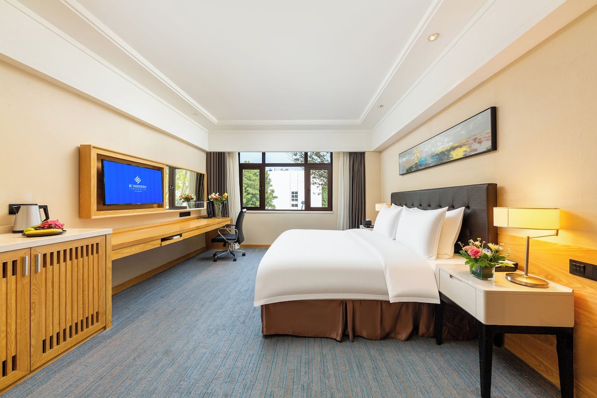 A hotel room with a bed, a desk, a television, and a window.
