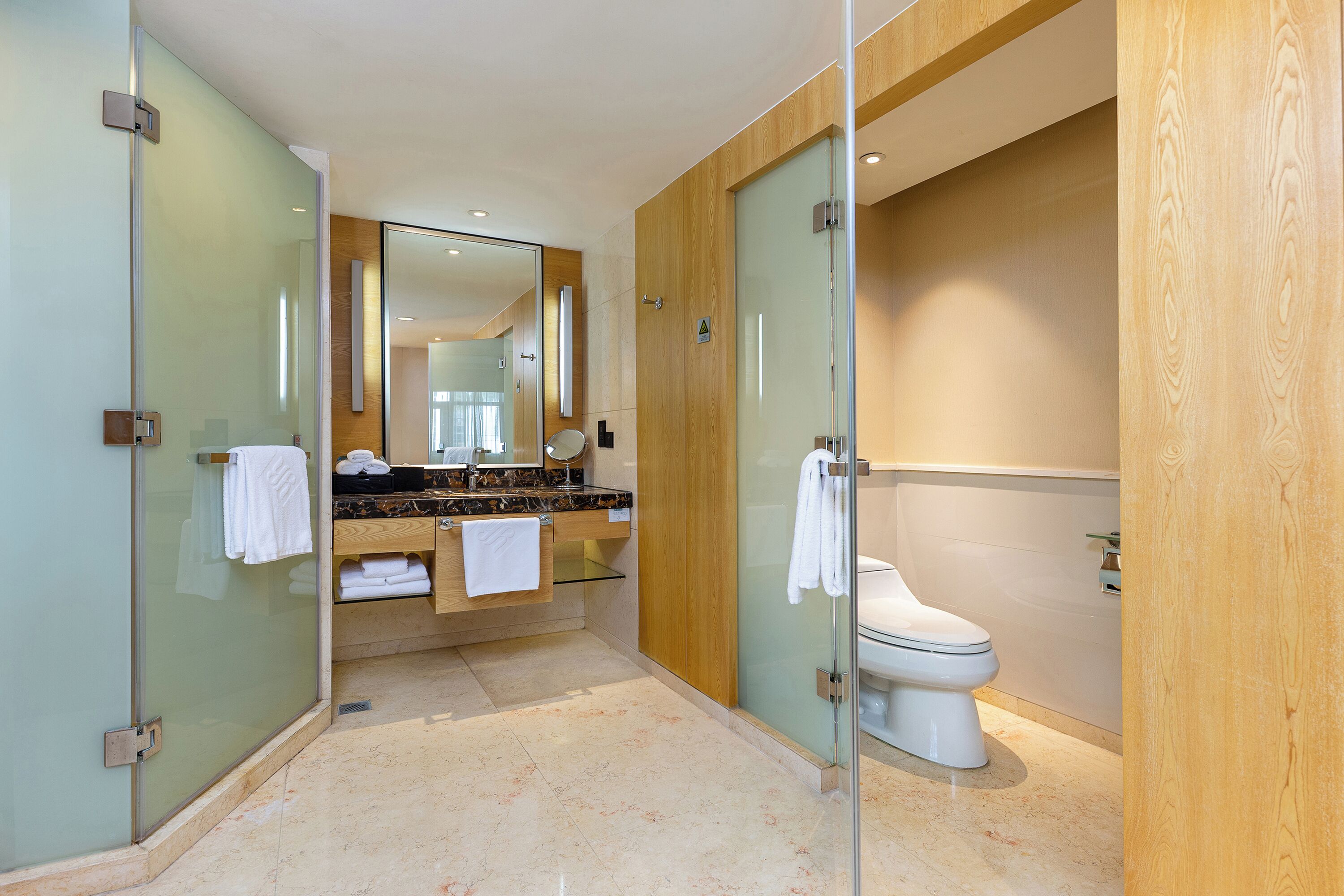 Et moderne badeværelse med et glasbadeværelse, et trækommode og et hvidt toilet.
