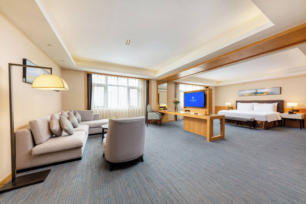A hotel room with a sofa, armchair, desk, television, bed, and bedside tables.