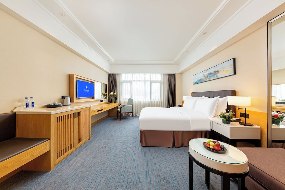 A hotel room with a bed, desk, chair, and a small table with fruit.