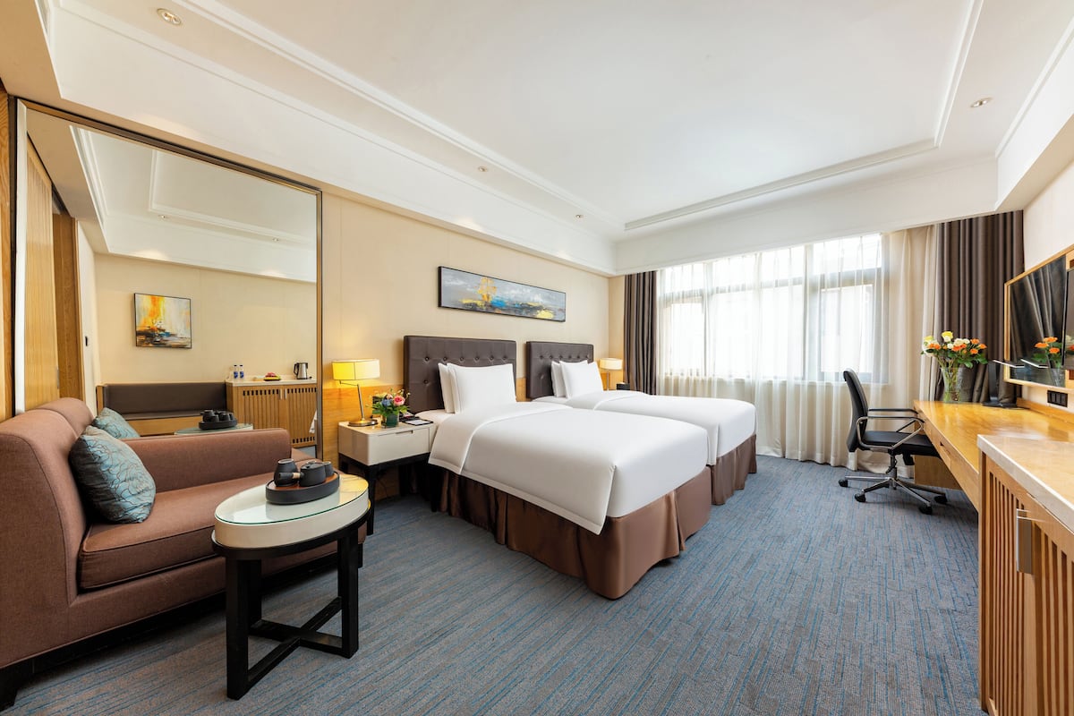 A hotel room with a sofa, two beds, a desk, a chair, and a large mirror.