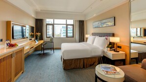 Habitación de hotel con cama, escritorio, silla, televisor y ventana con vista a la ciudad.