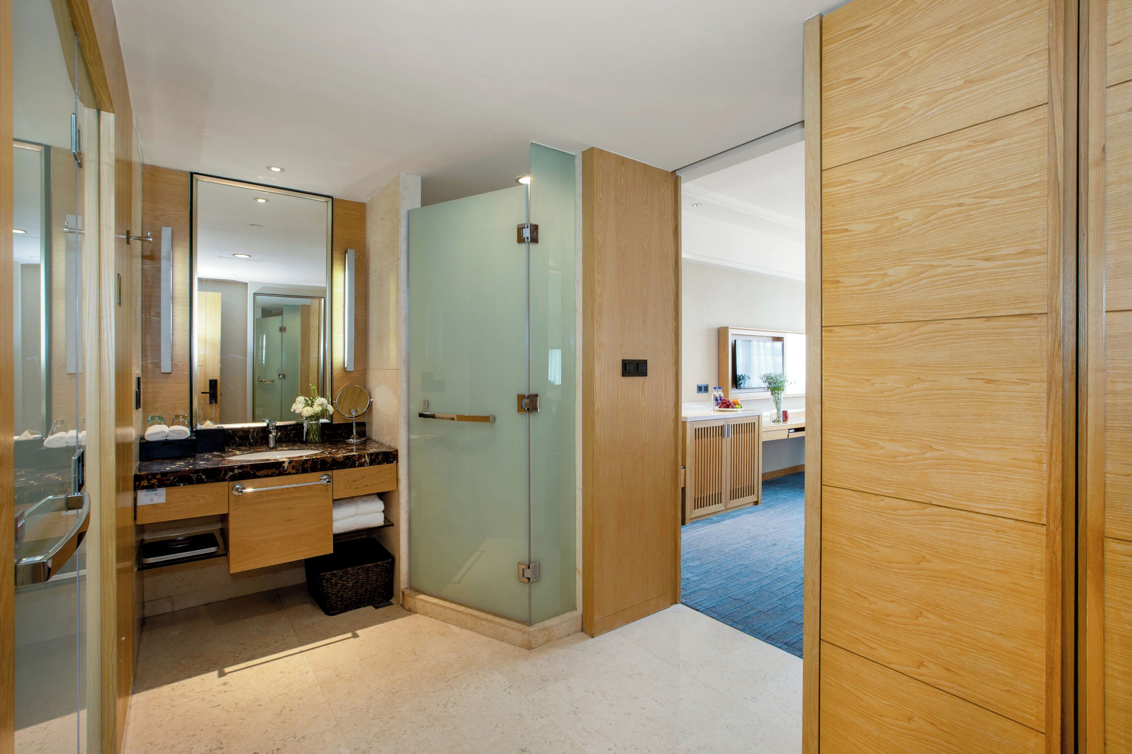 A modern bathroom with a glass shower enclosure, a marble countertop, and a wooden vanity.