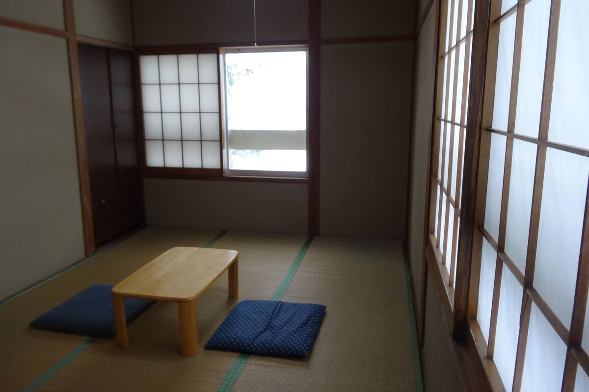 Una habitación japonesa tradicional con suelo de tatami, una mesa de madera baja y cojines azules.
