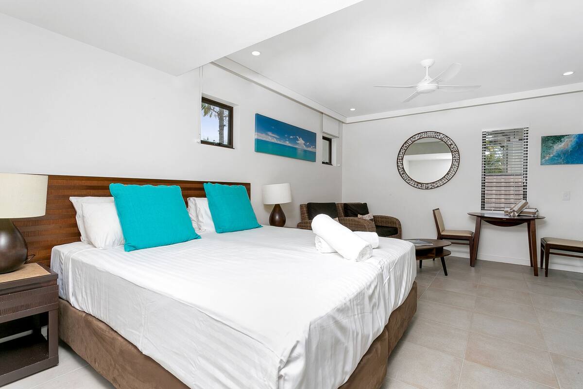 Habitación de hotel con una cama grande, un escritorio, una silla, un espejo redondo y dos cuadros colgados en la pared.