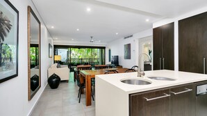 Een moderne keuken met een centraal eiland, ingebouwde apparatuur en een eethoek met uitzicht op groen.