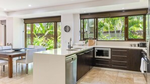 Een moderne keuken met een centraal eiland, inbouwapparatuur en grote ramen met uitzicht op een tropische tuin.