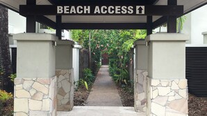 Een pad dat naar een toegangspunt tot het strand leidt, begrensd door stenen pilaren en weelderige begroeiing.