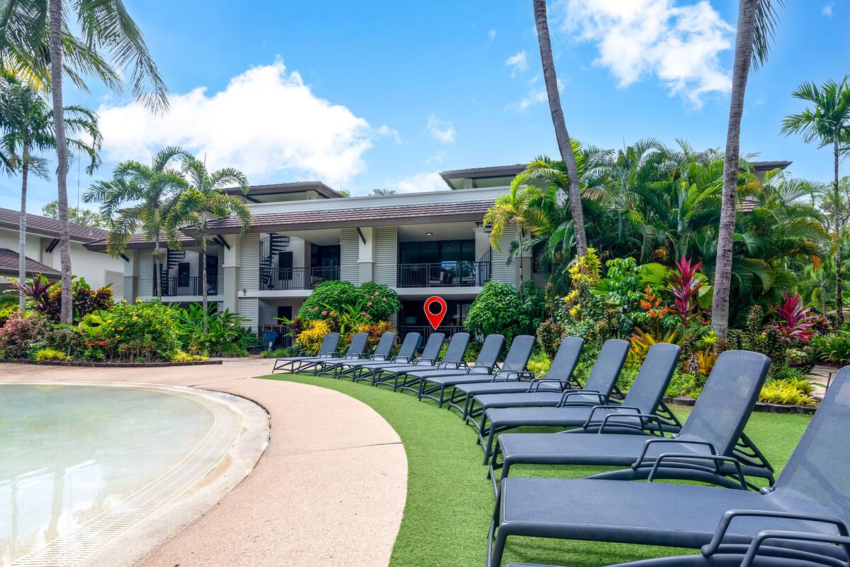 Zona junto a la piscina con sillones, una piscina y un edificio con balcones.