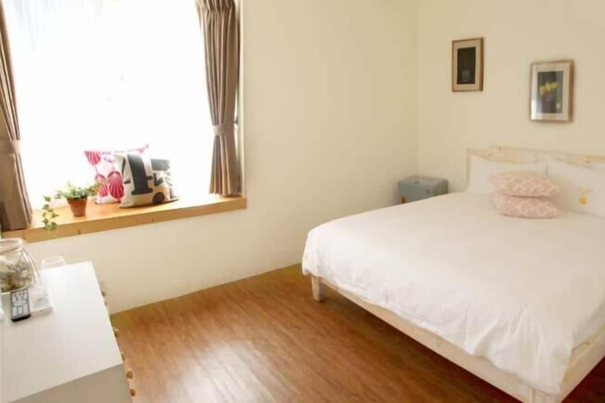 A bedroom with a bed, a bedside table, a window with curtains, and a small bedside lamp.