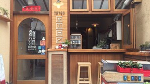 Une devanture de magasin en bois avec une enseigne indiquant « TETSU » et des icônes représentant les services proposés, tels que le thé, les gâteaux, le brunch, l’hébergement et les cours de surf.