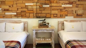 Une pièce avec deux lits, un mur en bois, une petite table sur laquelle se trouve une cage à oiseaux et un tapis vert.
