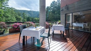 Uma área de refeições ao ar livre com mesas e cadeiras, cercada por um deck de madeira e plantas em vasos.