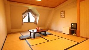 Um quarto tradicional japonês com piso de tatame, uma mesa baixa com um conjunto de chá, uma televisão e um pequeno frigorífico.