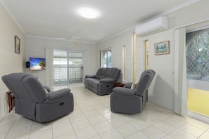 A living room with two grey reclining sofas, a flat-screen TV, and a ceiling fan.