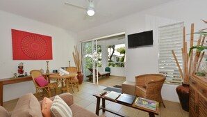 A living room with a sofa, a coffee table, and a dining area with chairs. There is a sliding glass door leading to an outdoor patio. - Seascape Holidays at Portsea (Port Douglas)