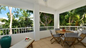 A covered patio with a table and chairs, a bench, and a large green vase. - Seascape Holidays at Portsea (Port Douglas)