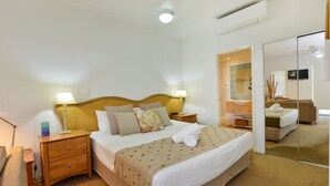 A well-lit bedroom with a large bed, bedside tables, a mirror, and a TV. - Seascape Holidays at Portsea (Port Douglas)