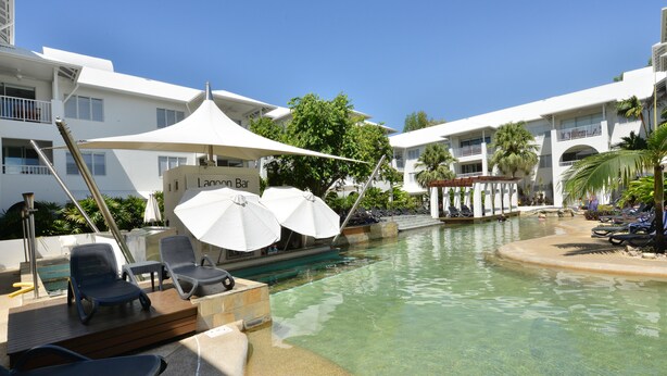 A pool area with lounge chairs and umbrellas, a small pool, and a building with balconies. - Seascape Holidays at Portsea (Port Douglas)