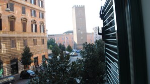 Vista de uma rua urbana com edifícios históricos, uma torre imponente e carros estacionados.