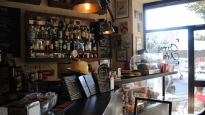 Uma área de bar com diversas garrafas de bebidas, um cardápio em lousa e uma exposição de café.