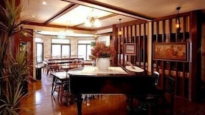 A dining area with wooden paneling, a piano, and a large vase of flowers. - Pension Marionette (Hakuba)