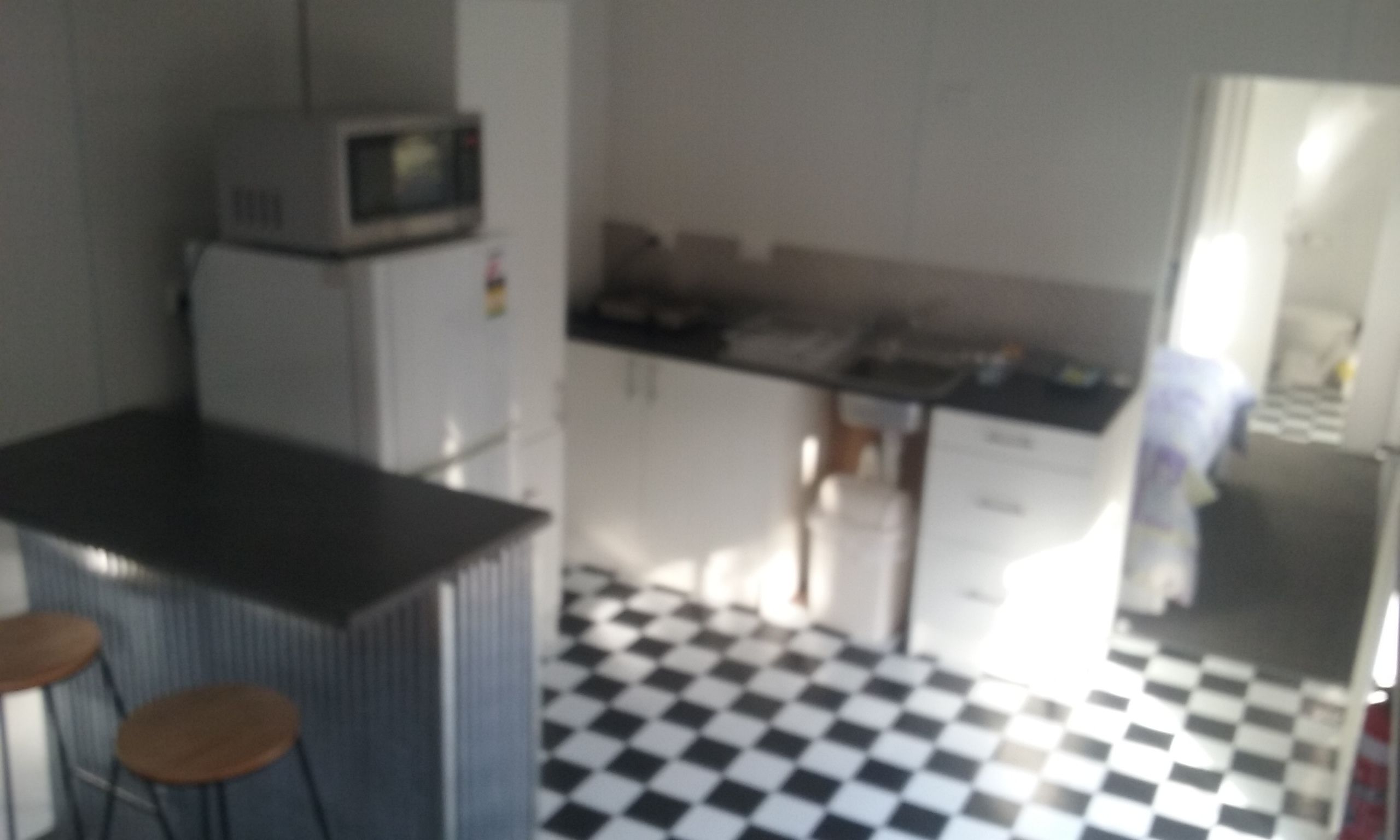Keittiössä on mustavalkoruudullinen lattia, mikroaaltouuni ja baaritiski jakkaroineen.