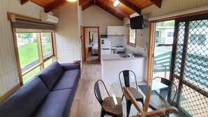 A cozy room with a sofa, a dining table with chairs, a kitchen area, and a large window. - G'day Parks Ararat (Ararat)
