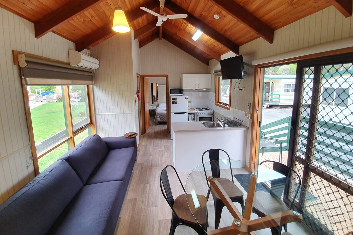 A cozy room with a sofa, a dining table with chairs, a kitchen area, and a large window.