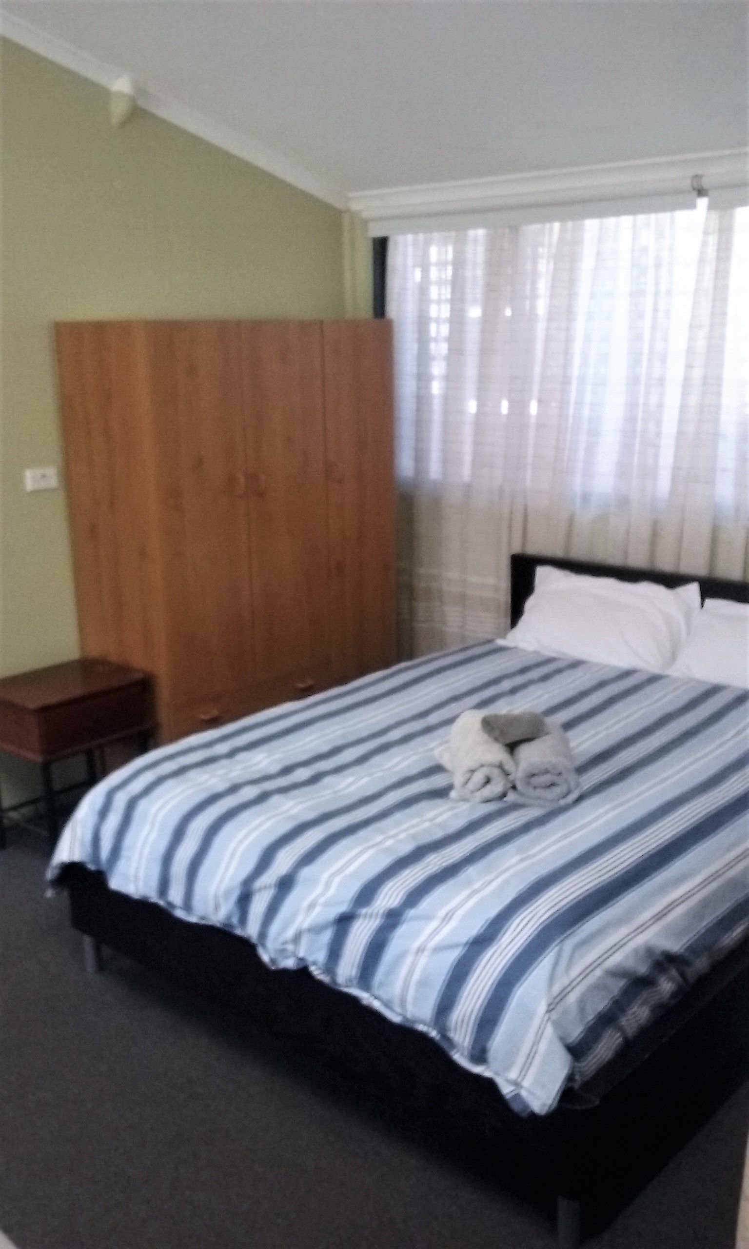 Habitación de hotel con cama, armario de madera, una mesita y ventana con cortinas.