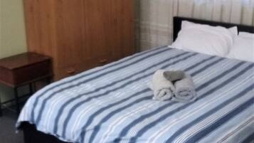 Habitación de hotel con cama, armario de madera, una mesita y ventana con cortinas.