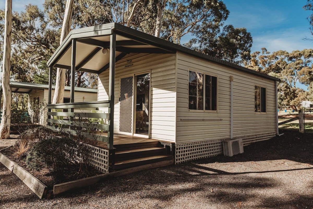 A small, single-story mobile home with a covered porch and a fenced garden area.