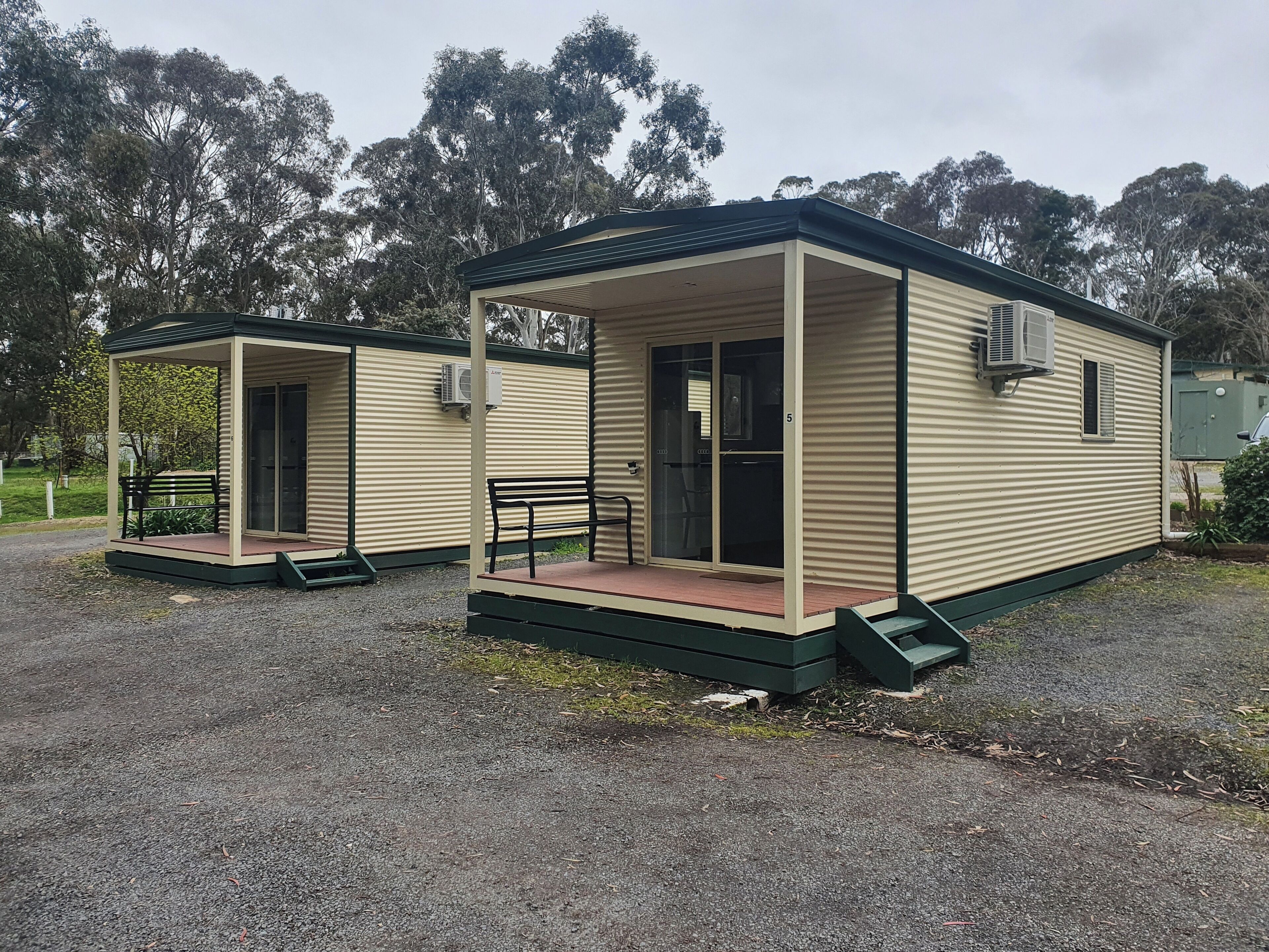 Two small, single-story cabins with a covered porch and a bench. Each cabin has a sliding glass door and an air conditioning unit mounted on the exterior wall.