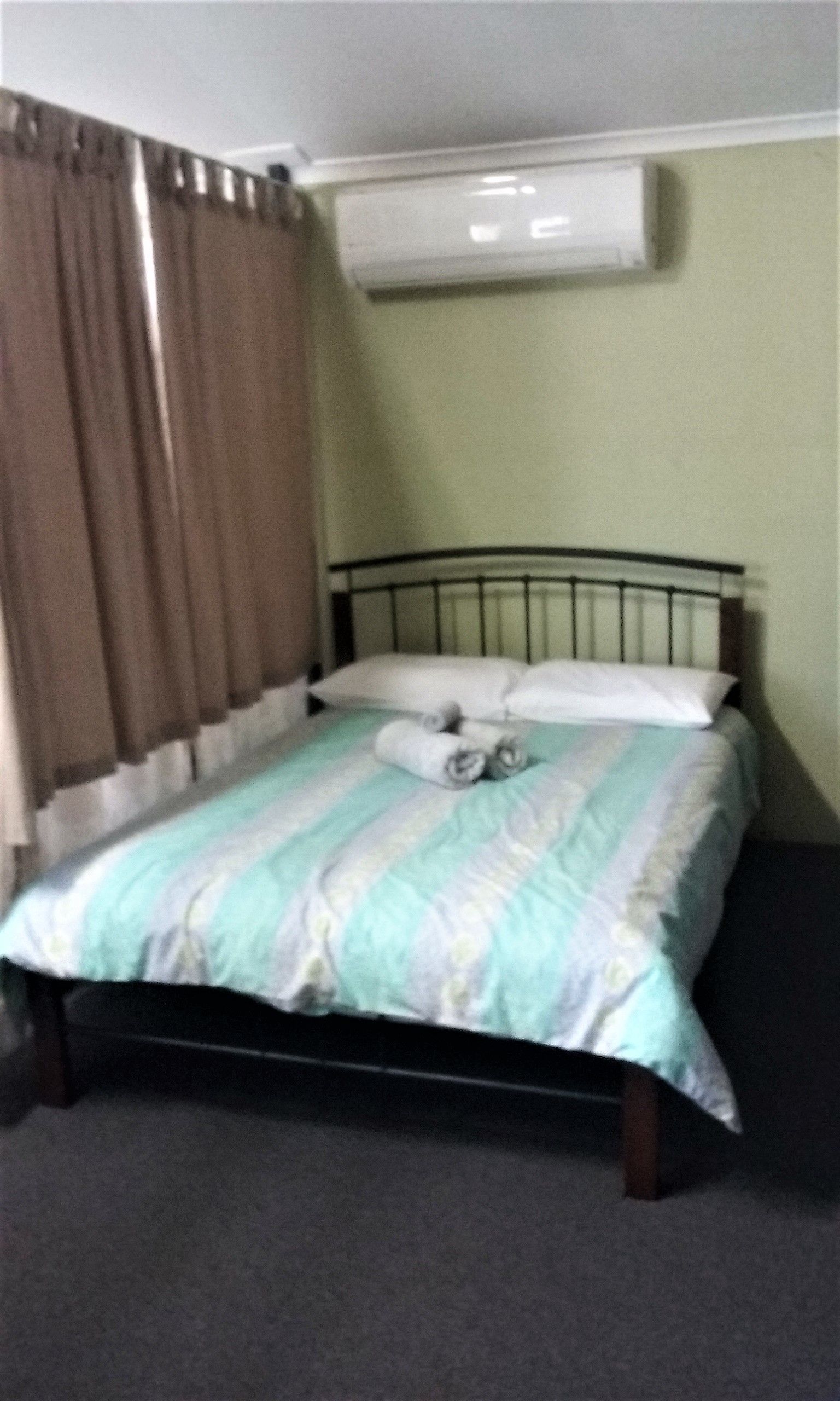 Uma cama de solteiro com colcha listrada, dois toalhas enroladas e uma almofada branca.