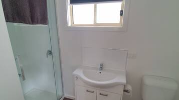A bathroom with a glass shower enclosure, a white sink with a window above, and a toilet.